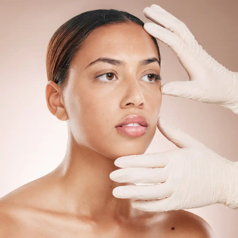 Woman’s face framed by gloved hands examining her skin.